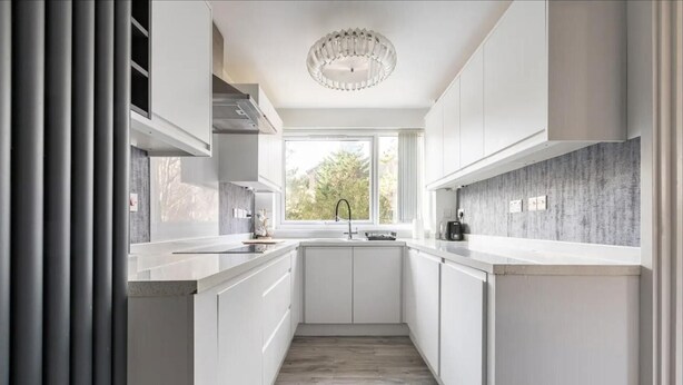 A modern kitchen with white cabinetry, a central island, and a window providing natural light. - Spacious 1 bed Apartment With Parking & Balcony! (Bromley)