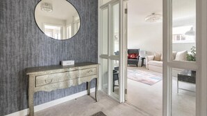 A modern living room with a grey textured wall, a round mirror, a wooden console table, and a sliding glass door leading to an outdoor area. - Spacious 1 bed Apartment With Parking & Balcony! (Bromley)