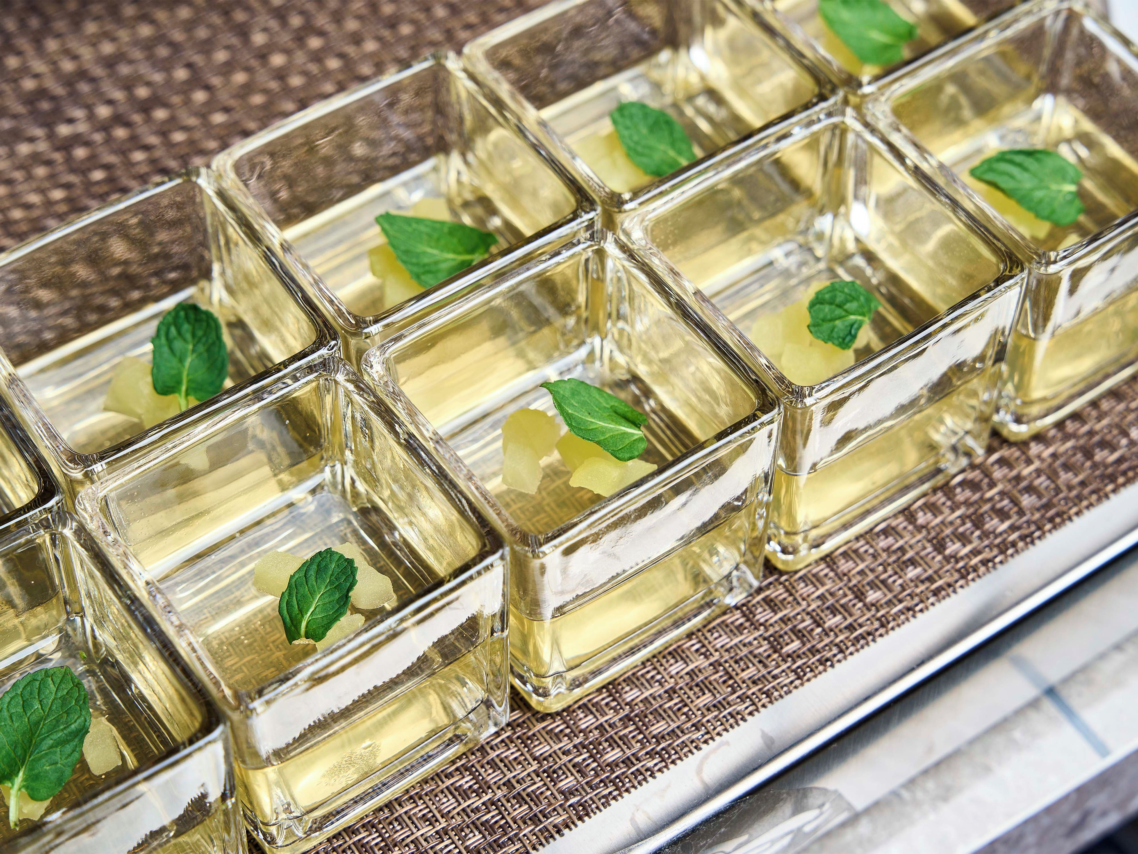 Un vassoio con cubetti di vetro trasparente contenenti un liquido giallo, probabilmente una bevanda, e foglie di menta.