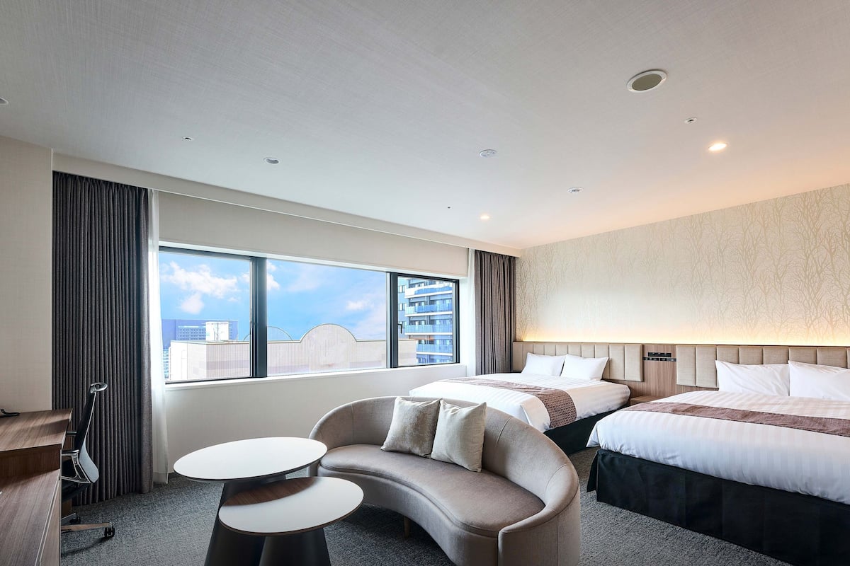 Ein Hotelzimmer mit einem großen Bett, einer Sitzecke, einem Schreibtisch und Blick auf die Stadt.