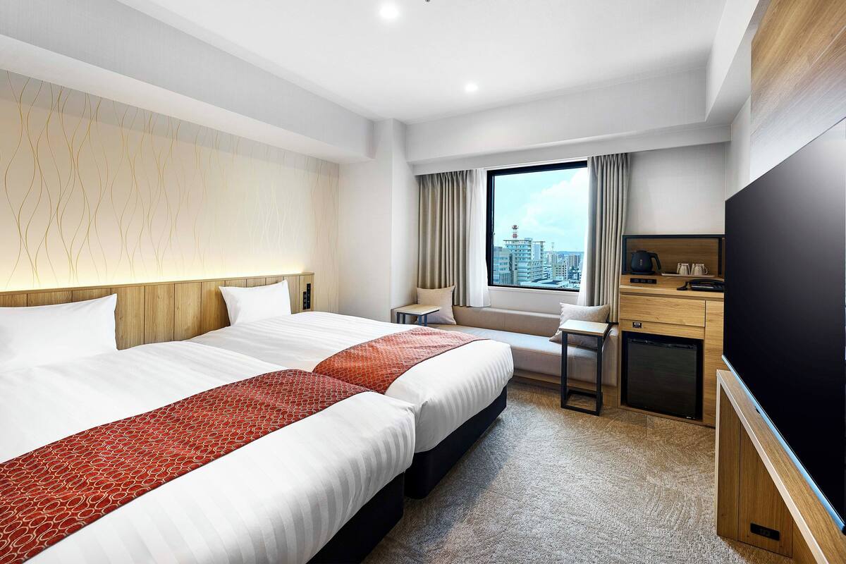 Ein Hotelzimmer mit einem großen Bett, einem Schreibtisch, einem Fernseher und einem Fenster mit Blick auf die Stadt.