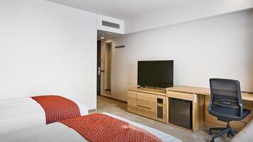 Quarto de hotel com cama, escrivaninha, cadeira, televisão e guarda-roupa.