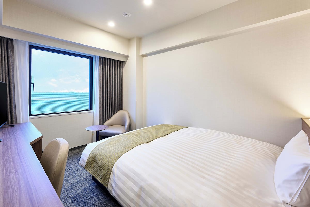 Ein Hotelzimmer mit Bett, Schreibtisch, Stuhl, einem Fenster mit Vorhängen und Meerblick.
