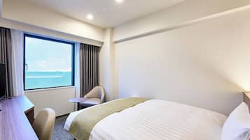 Een hotelkamer met een bed, een bureau, een stoel, een raam met gordijnen en uitzicht op zee.