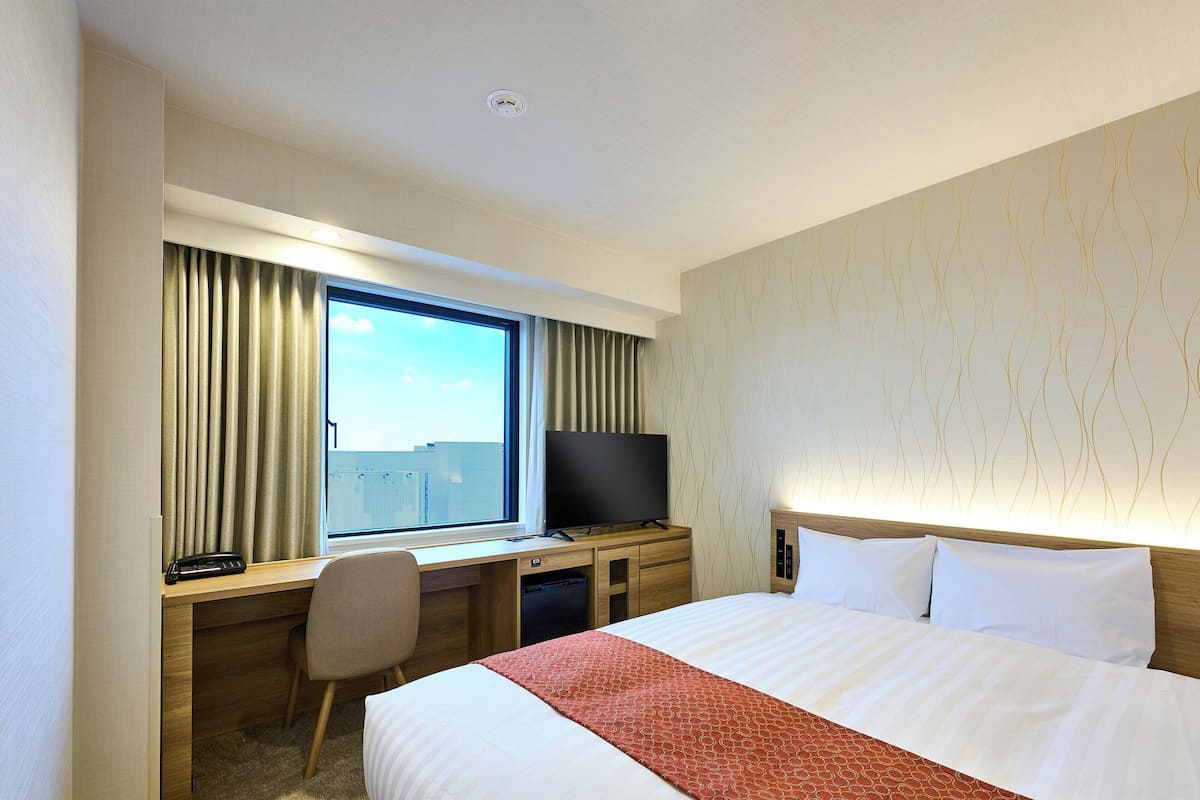 Ein Hotelzimmer mit einem großen Bett, einem Schreibtisch mit Computer, einem Fernseher und einem Fenster mit Vorhängen.