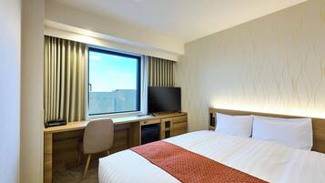 A hotel room with a large bed, a desk with a computer, a television, and a window with curtains.