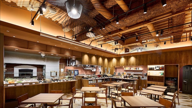 Un restaurante espacioso con varias mesas y sillas, un área de cocina y una variedad de alimentos exhibidos.