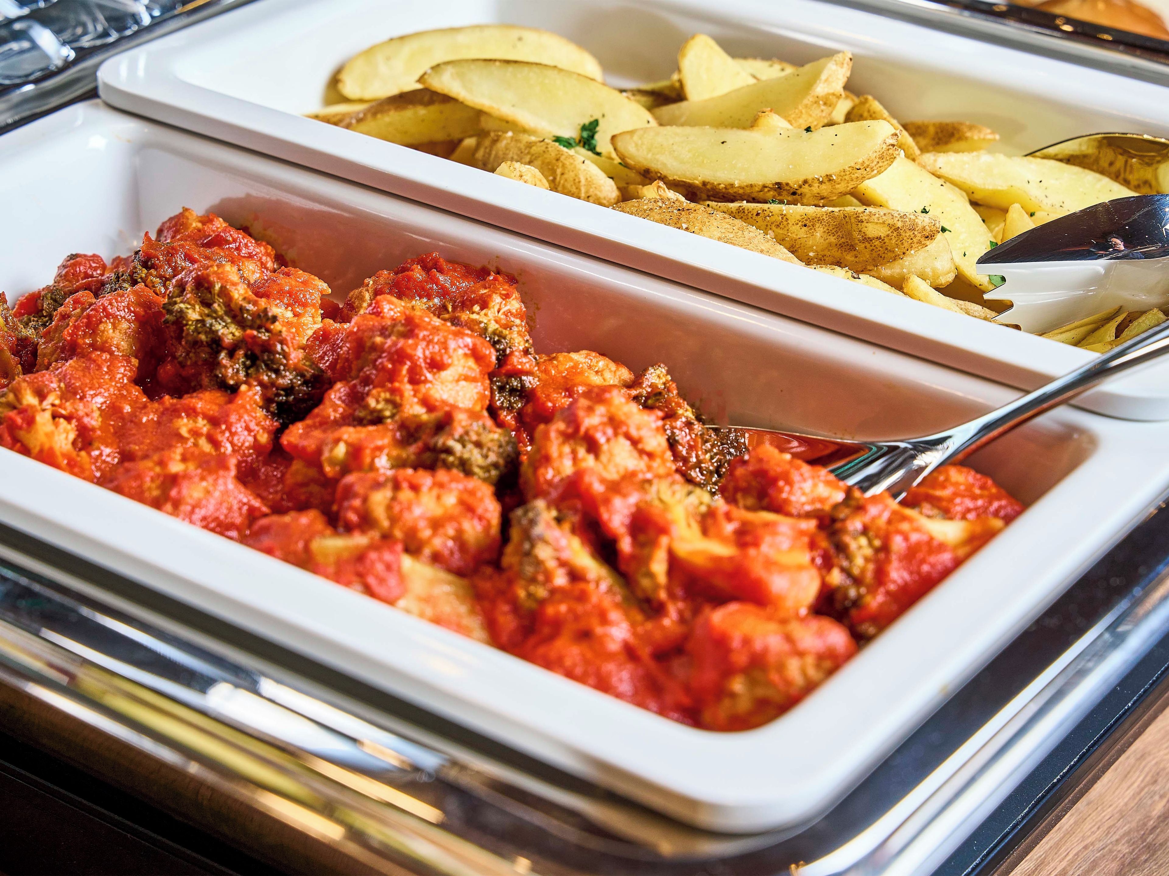 A buffet with a variety of dishes including a red sauce with meat, and sliced potatoes.