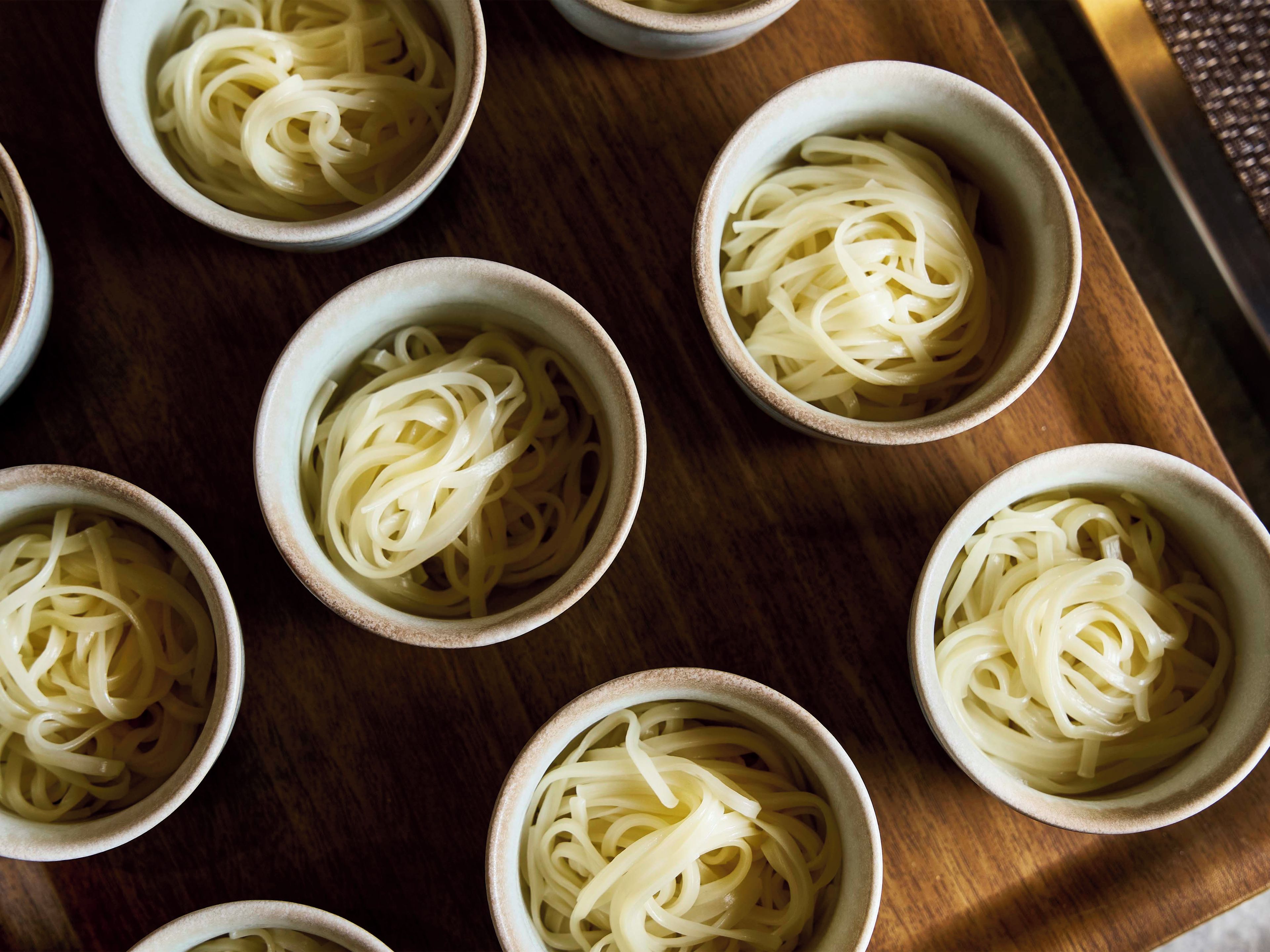 Multiple bowls of pasta arranged on a wooden surface.