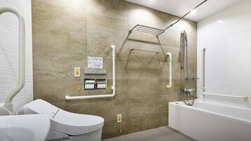 Une salle de bain moderne équipée d’une baignoire, de toilettes et d’un lavabo. Elle comprend également des barres d’appui et un siège de douche pour faciliter l’accès aux personnes à mobilité réduite.