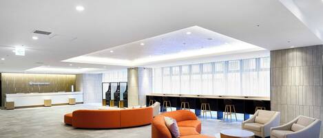 A modern hotel lobby with a reception desk, seating area, and large windows.