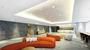 Un lobby moderno de hotel con un sofá naranja curvo, un mostrador de recepción y una zona de bar.
