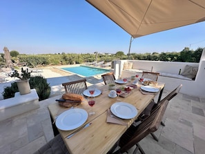 Mesa de jantar montada ao ar livre, com piscina ao fundo.