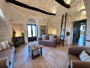 Uma sala de estar aconchegante com parede de pedra, escada de madeira, sofá, mesa de centro e estante.