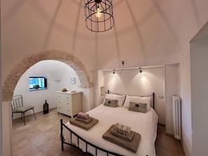 Quarto com uma cama grande, cômoda, cadeira e um arco de pedra.