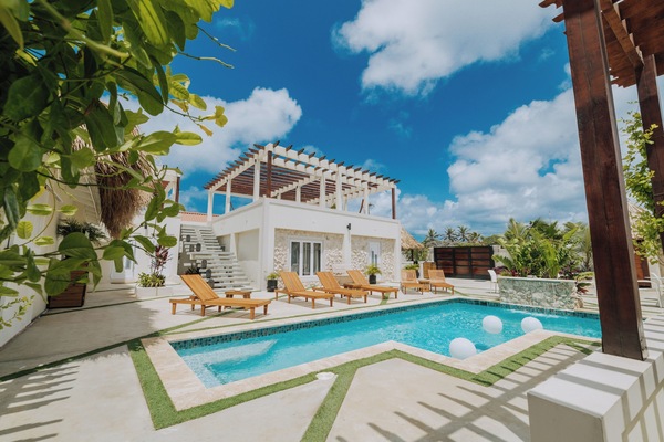 Relax under the Caribbean sun by the stunning pool, surrounded by lush greenery and modern outdoor seating.