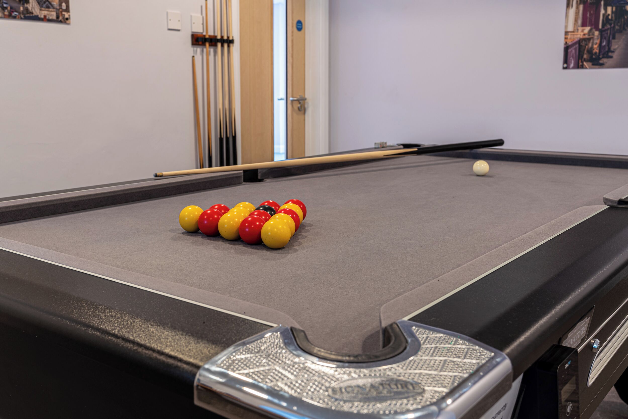 A pool table with balls and cues, a door, and a wall with a picture.