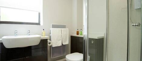 A modern bathroom with a glass shower enclosure, a white toilet, and a black vanity with a sink.