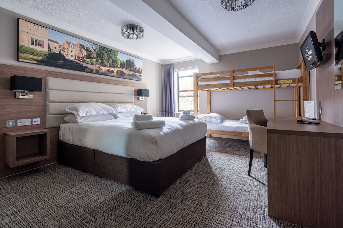 A hotel room with a bed, a desk, a TV, and a painting of a town.