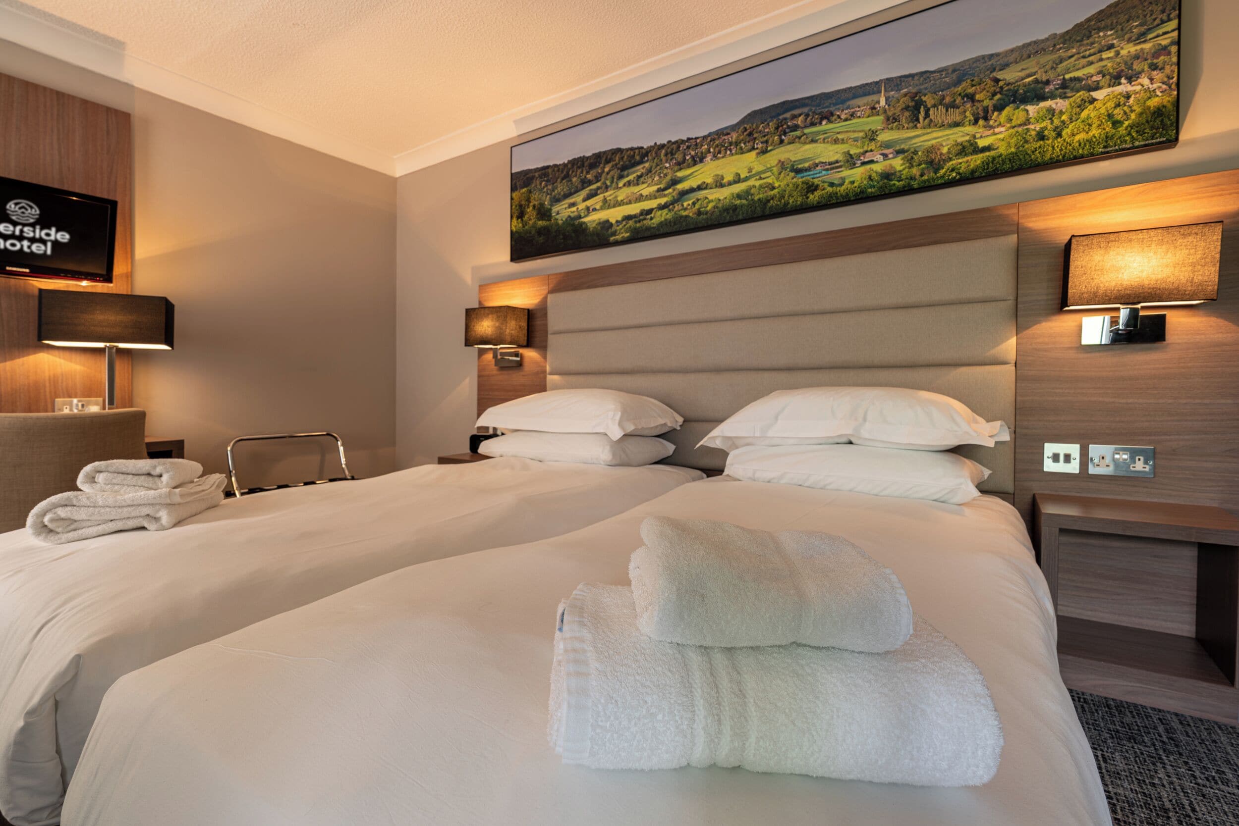 A hotel room with two beds, a flat-screen TV, and a painting of a landscape.
