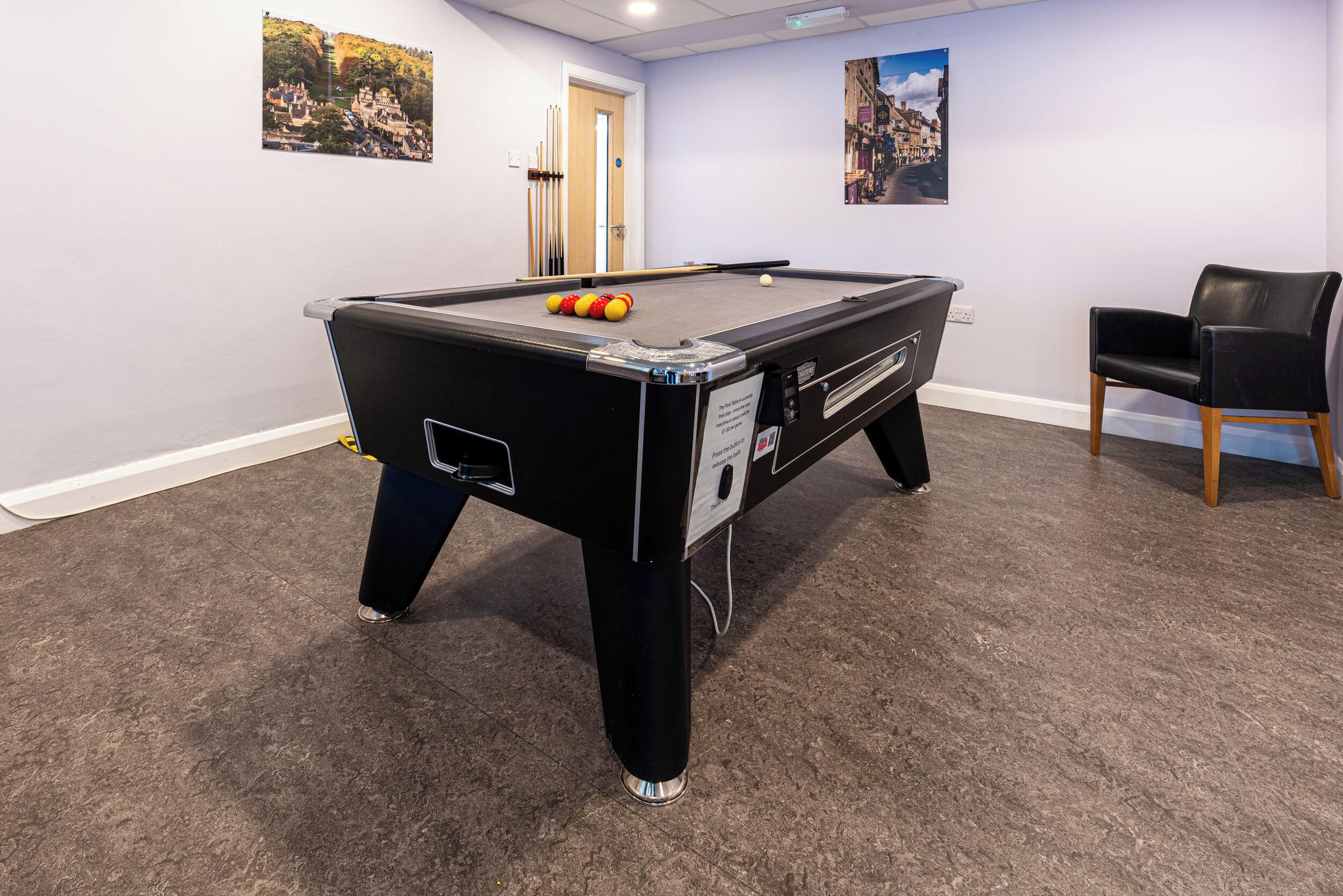 Une table de billard avec des billes, une chaise et deux tableaux encadrés accrochés au mur.