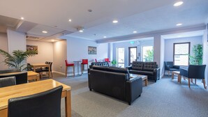 A modern lounge area with seating, tables, and plants. - Riverside Hotel (Cirencester)