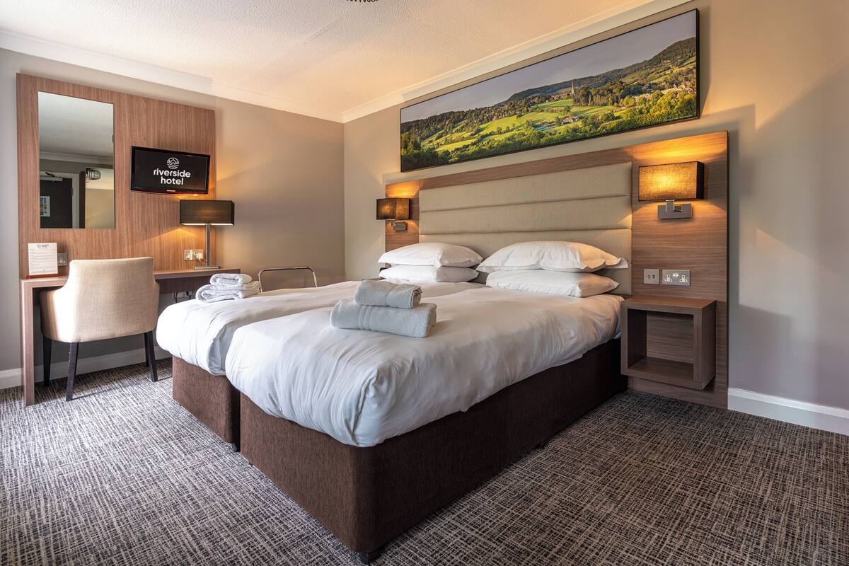 A hotel room with a large bed, a desk, a chair, a TV, and a painting on the wall.