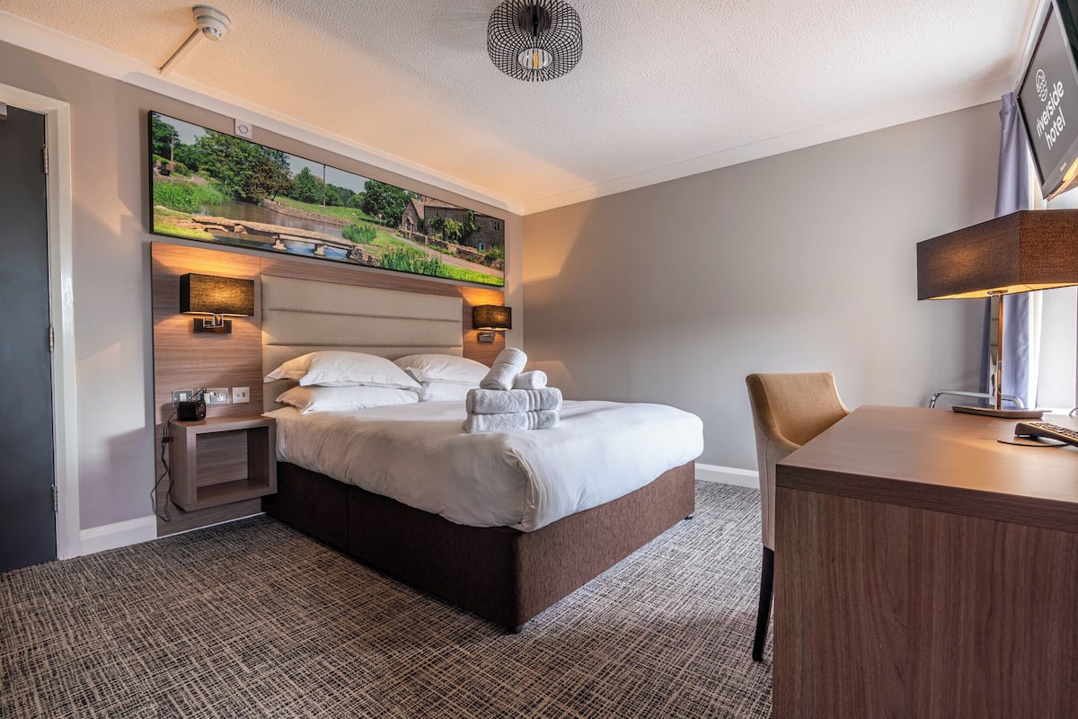 A hotel room with a large bed, bedside tables, a desk, and a painting above the bed.