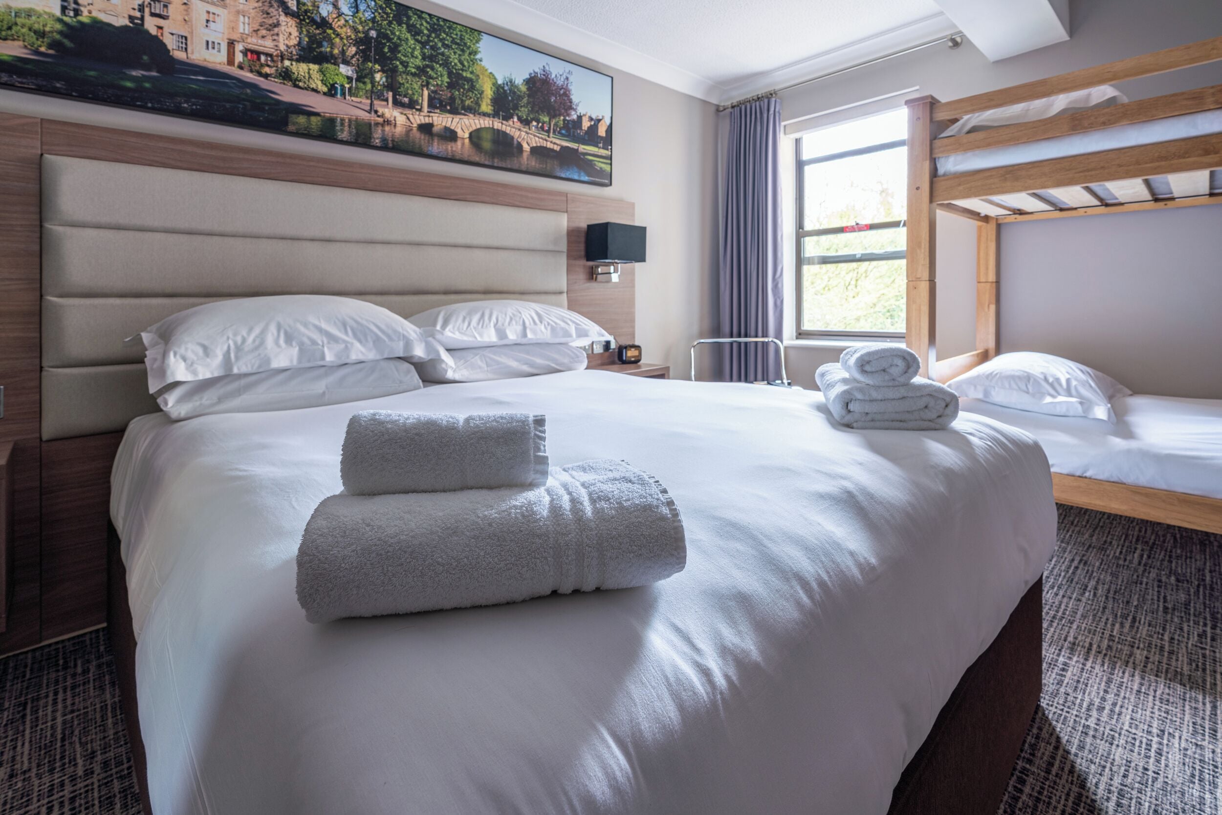A hotel room with a large bed, a smaller bed, a TV, and a painting of a bridge.