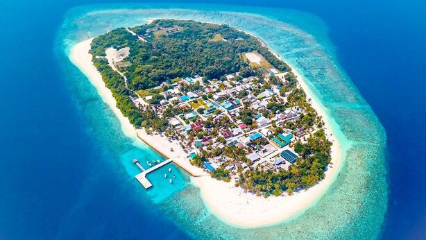 Una vista aerea di una piccola isola con un fitto gruppo di edifici, un molo e acque cristalline.