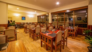 A restaurant with wooden tables and chairs, a bar area, and large windows. - Hotel Chiminda Pelling (Gyalshing)