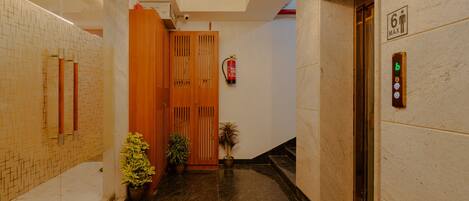 A modern elevator with a digital display, a fire extinguisher mounted on the wall, and a wooden door with a vertical slat design.