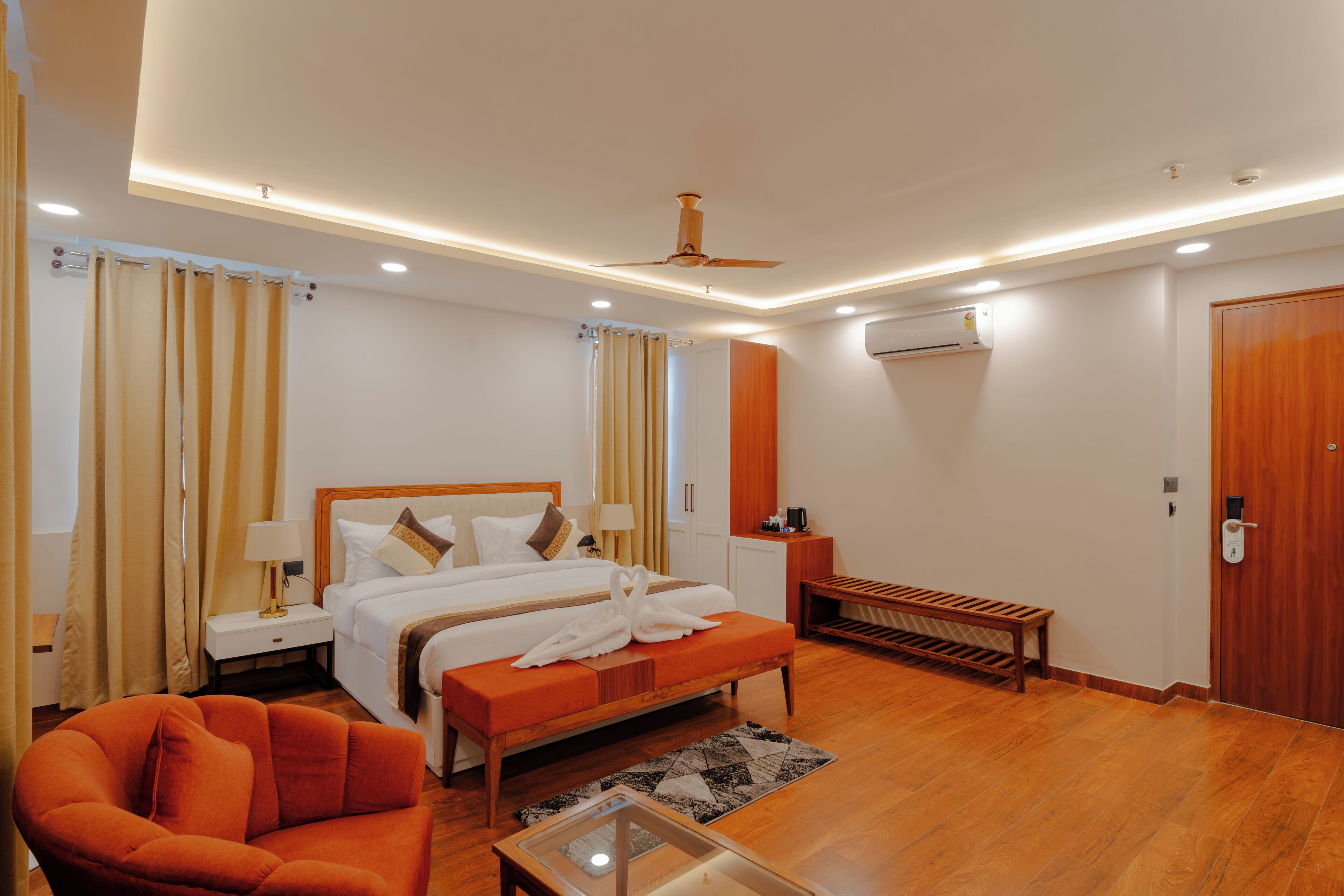 Una habitación de hotel moderna con una cama grande, un banco de madera, una mesita pequeña y un ventilador de techo.