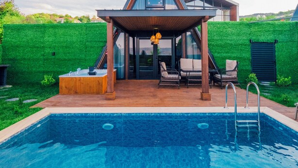 Ein modernes Haus mit Swimmingpool, einer überdachten Terrasse mit Sitzgelegenheiten und einer grünen Wand.