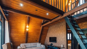 Ein großzügiger Loft mit hoher Decke, Holzbalken, einer Treppe, einer Couch, einem Couchtisch und einem an der Wand befestigten Flachbildfernseher.