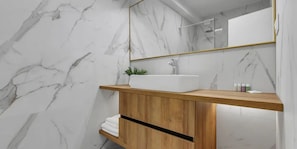 Ein Badezimmer mit einer Marmorwand, einem Holzwaschtisch, einem weißen Waschbecken und einem Spiegel mit goldener Rahmung.