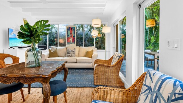 Un salon moderne avec une table à manger, des meubles en osier et de grandes fenêtres donnant sur l’extérieur.