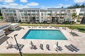 A modern hotel with a central swimming pool surrounded by sun loungers and a well-maintained lawn.
