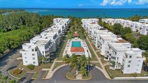 A resort with multiple white buildings, a central pool, and a view of the ocean.