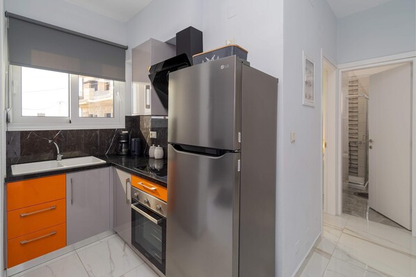 Una cocina moderna con un refrigerador de acero inoxidable, un horno empotrado y armarios color naranja.