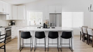 A modern kitchen with white cabinetry, a central island with bar stools, a stainless steel refrigerator, and a dining area with chairs. - Scottsdale Escape by LuxeKey | 4BDs Near Mayo Clinic & Kierland w/Pool (Scottsdale)