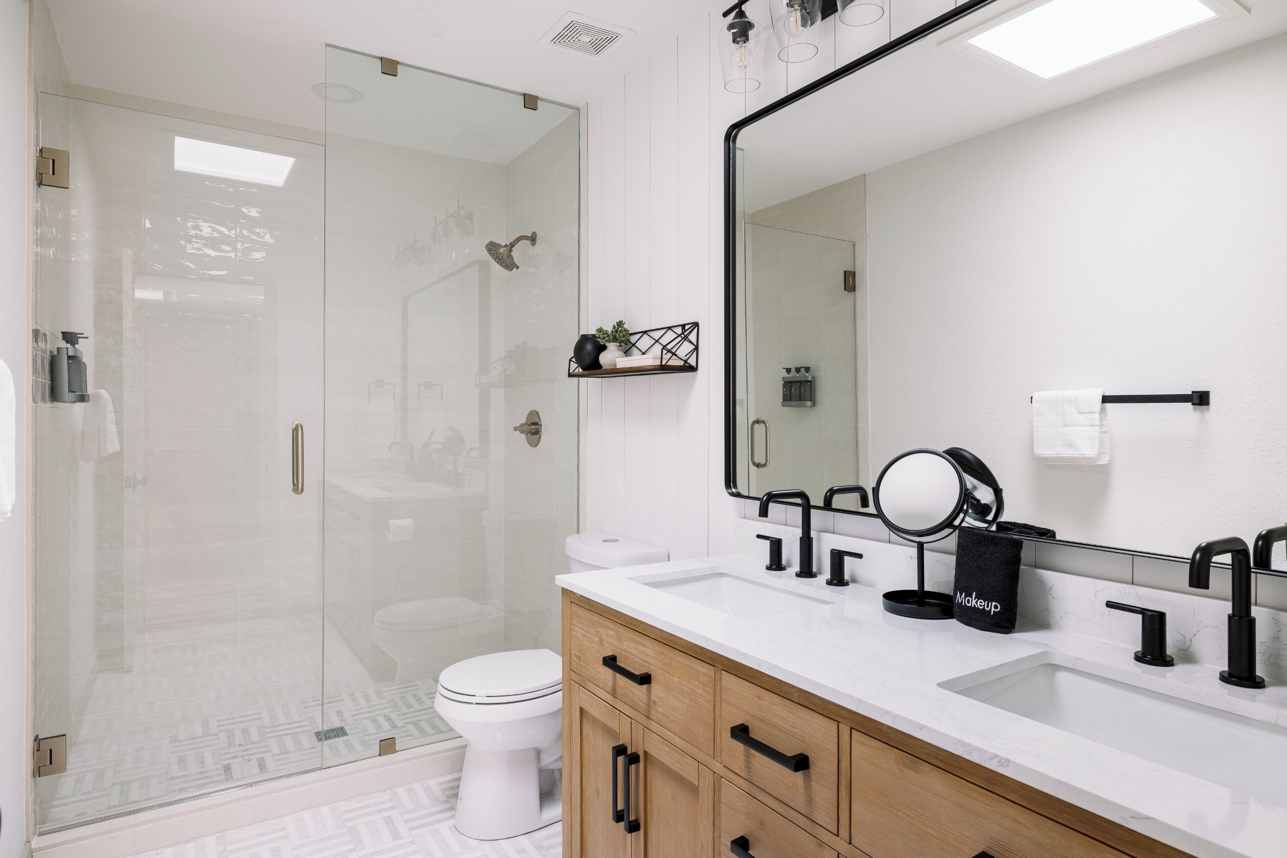 Un baño moderno con ducha envuelta en vidrio, inodoro blanco, tocador con espejo y lavamanos.