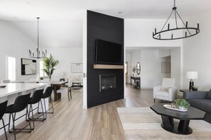 A modern living room with a fireplace, a dining area with a long table and chairs, and a black accent wall with a flat-screen TV. - Scottsdale Escape by LuxeKey | 4BDs Near Mayo Clinic & Kierland w/Pool (Scottsdale)