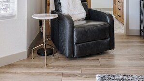 A modern living room with a black leather chair, a small round table, and a floor lamp. A wooden sliding door leads to a bathroom. - Scottsdale Escape by LuxeKey | 4BDs Near Mayo Clinic & Kierland w/Pool (Scottsdale)