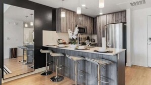 A modern kitchen with a central island, bar stools, stainless steel appliances, and pendant lighting.