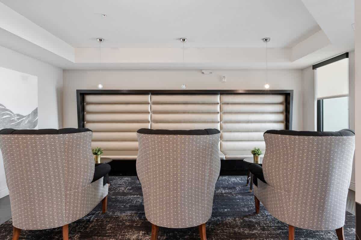 Quarto de hotel moderno com três poltronas estofadas, uma janela grande e um tapete escuro.