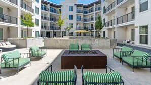 A modern outdoor patio area with multiple seating options, a central fire feature, and a view of the building's exterior.