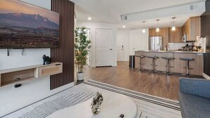 A modern kitchen with a central island, bar stools, and a large flat-screen TV mounted on the wall.