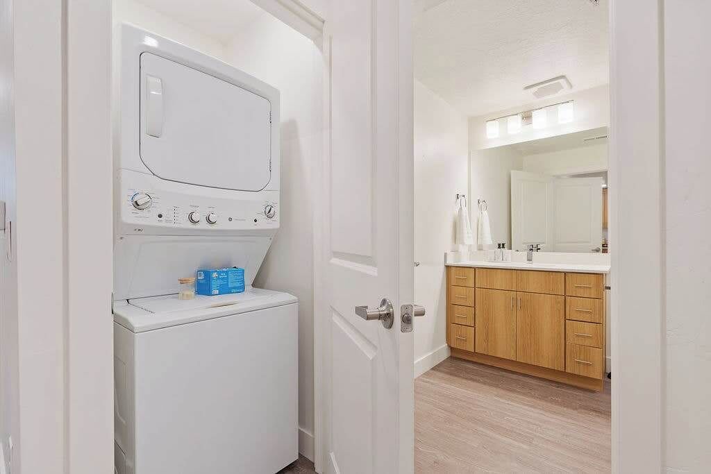 A laundry area with a washing machine and a drying rack, a wooden cabinet with a mirror, and a white door.