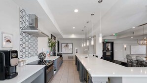 Une cuisine moderne dotée d’un grand îlot central, d’appareils électroménagers en acier inoxydable et de luminaires suspendus.